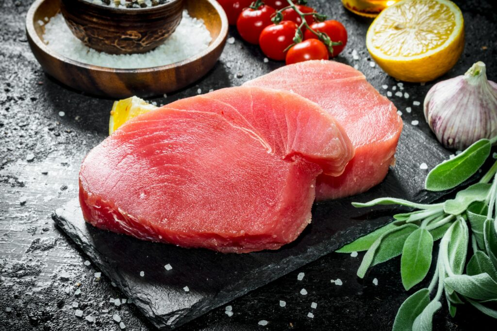 Raw tuna fillet on a stone Board with salvia and lemon.
